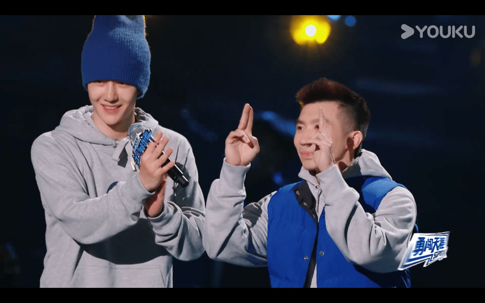 Yibo clapping for his friend Astro, who is making a saluting gesture in thanks to the audience with the first two fingers of each hand.