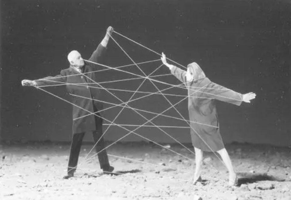A black and white image of an older man and an older woman entwined in a giant string cats cradle