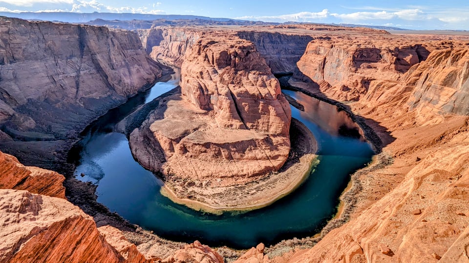An image of Horeshoe Bend, a meander of the Colorado River in Arizona. A river winds around tall, barren rocks, creating the appearance of a horsehoe