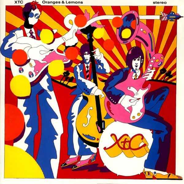 A cartoonish drawing of the members of XTC done in a psychedelic, YELLOW SUBMARINE (the movie) way. It's full of color, lots of reds, yellows, oranges and deep blues. One figure is playing a guitar, and the neck of the guitar is turning into the airstream of a jet fighter airplane. Another guitarist sits on a bass drum labled XTC. Behind them is a guy playing standup bass. There is a pink horn shooting out oranges and lemons behind them.