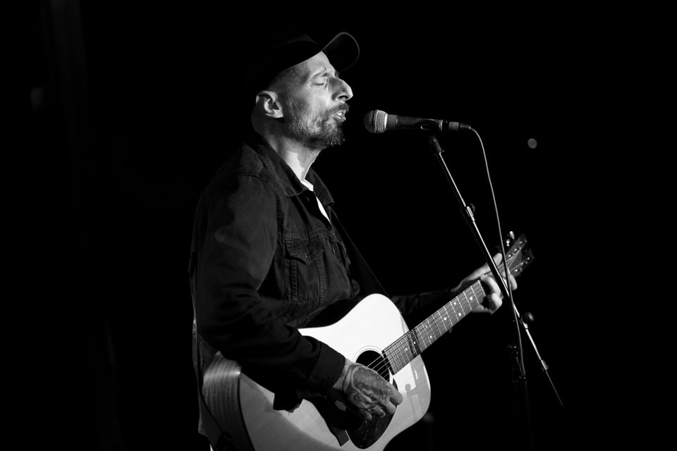 a man, Red At Night playing an acoustic guitar at Kick Butt Coffee, Austin TX in a live performance black and white photo