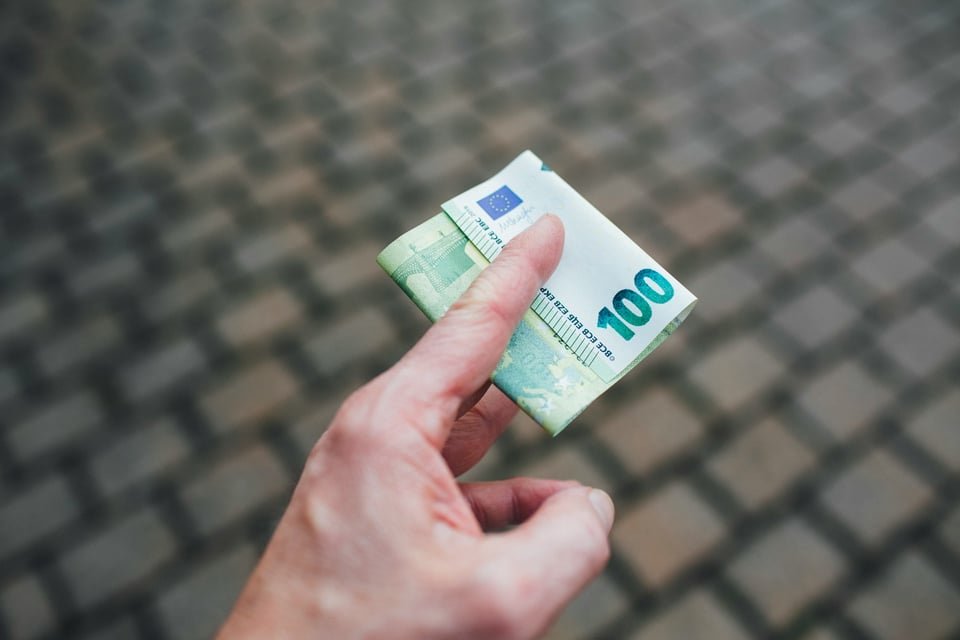 Image of a hand, holding a folded 100-Euro note. Photo by Markus Spiske on Unsplash.
