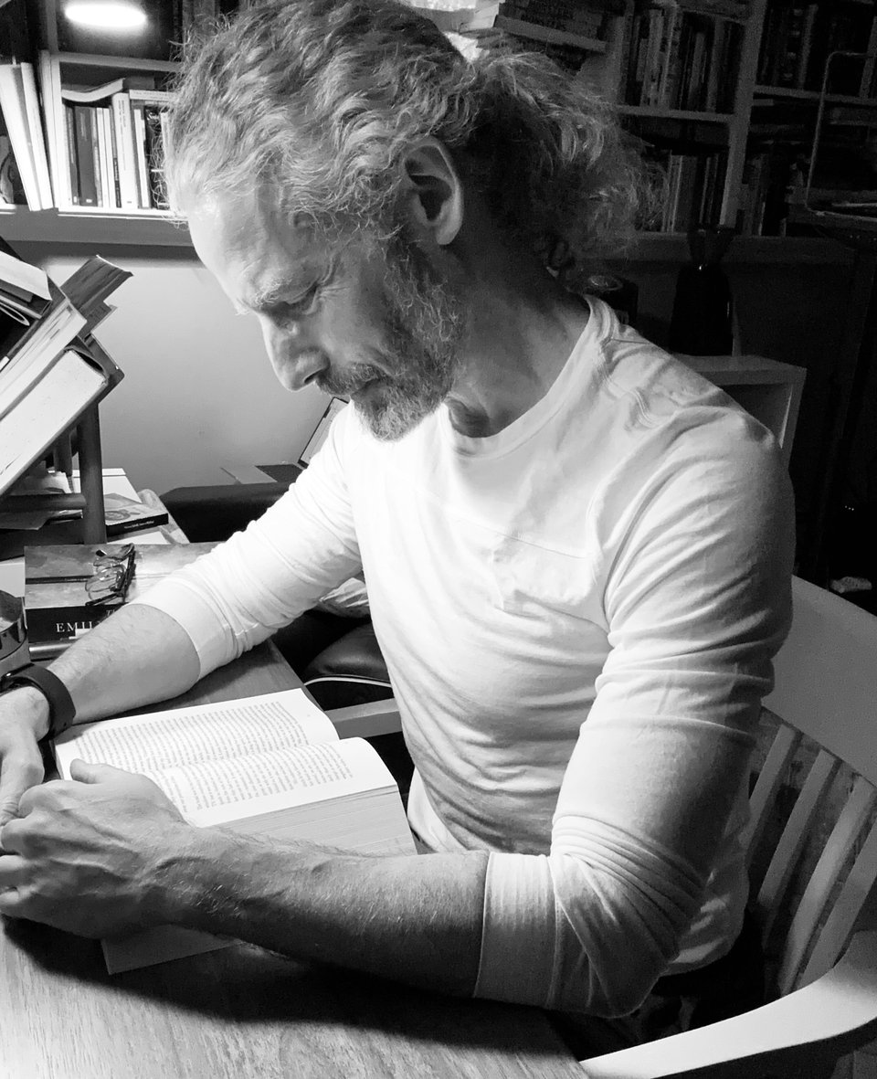 b/w photo of white man at a desk reading a thick paperback
