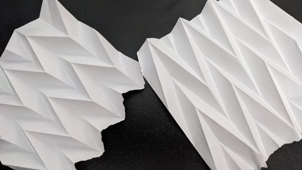 two pieces of paper on a black background, folded into a Miura-ori fold