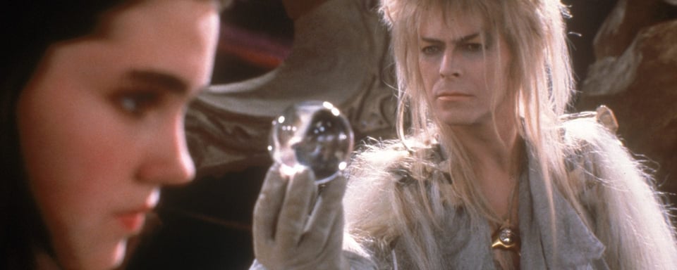 Image from the movie Labyrinth. David Bowie as goblin king Jareth is holding up a crystal ball to Sarah, played by Jennifer Connelly.