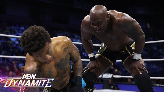 Shelton Benjamin stands over Lio Rush mockingly.