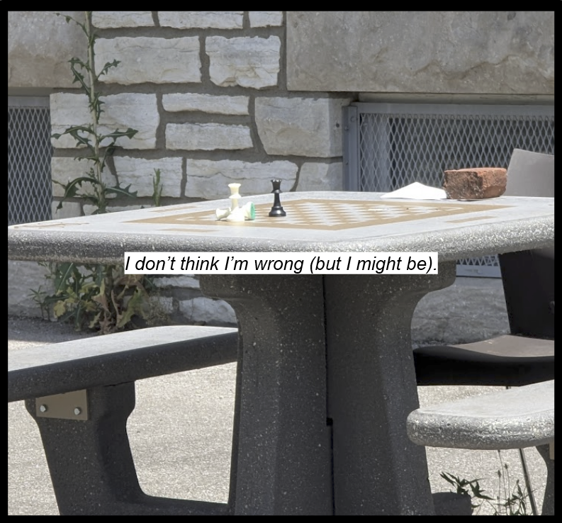 A concrete chessboard outside a concret building. A black queen and white queen face each other, and a second white queen is laid down. A brick holds a piece of paper on the opposite edge.