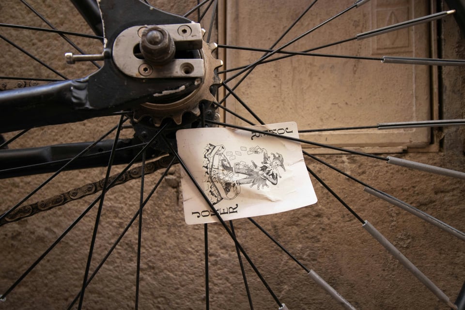 A Joker playing card caught in the spokes of a bicycle.