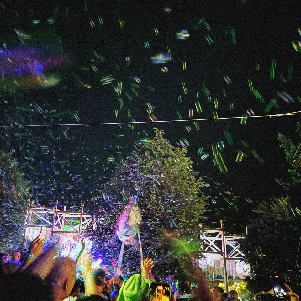 an enormous fish puppet emerges during a music festival proceeded by a machine putting out a ridiculous amount of bubbles