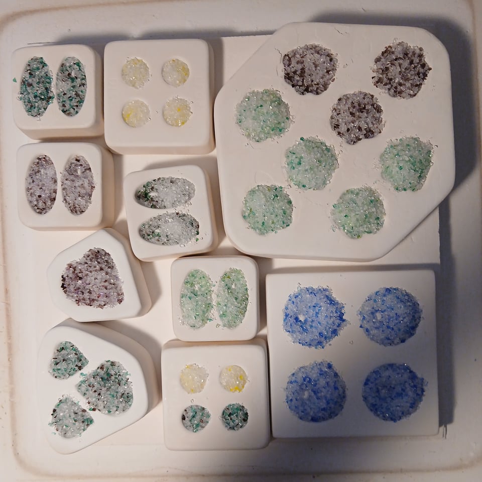 kiln shelf with molds in circle, oval, paw and heart molds, mostly in purples, greens, blues and yellows