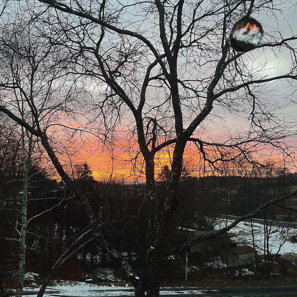 a sun rises over Greene County, NY - fiery up top, wintry down bottom, with a refracting crystal hanging in the window upper corner right