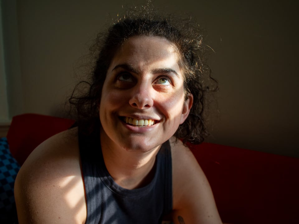 A portrait of Kat- mostly dark, but with patches of sunlight coming in through the window illuminating her eye and shoulder.