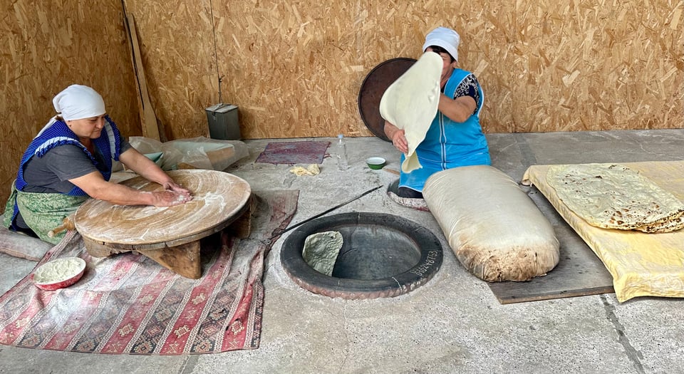 Two women making lavash flatbread in a traditional pit oven