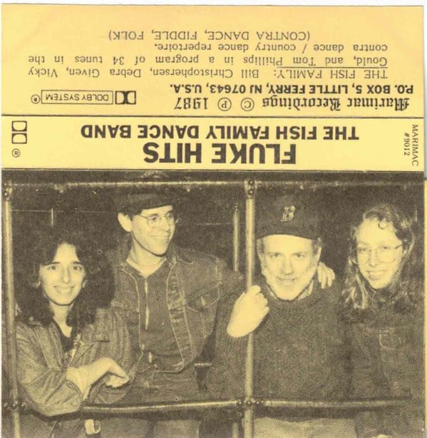 Scan of a cassette tape label. The album name, displayed upside down, is FLUKE HITS - THE FISH FAMILY DANCE BAND. The sleeve paper is either yellow or yellowed with age, and there is a black and white photograph of two women and two men in casual dress smiling at the camera.