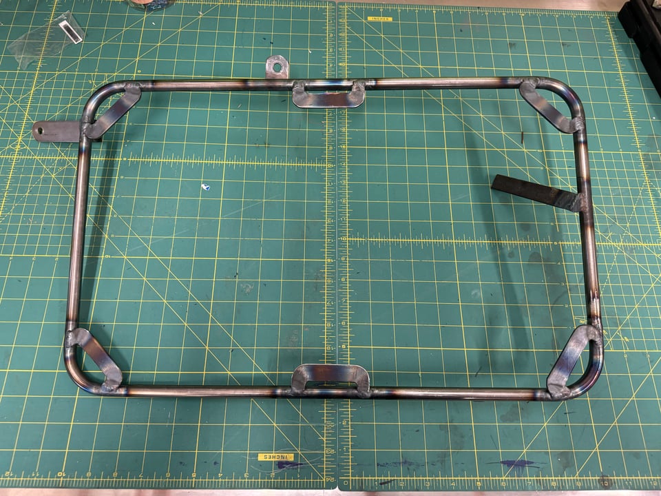 The luggage rack for the left side of the bike, isolated on a workbench.