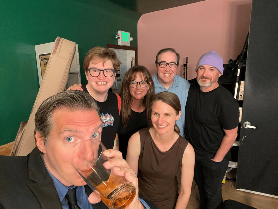 A man slurps a beer while taking a selfie with smiling, energized performers