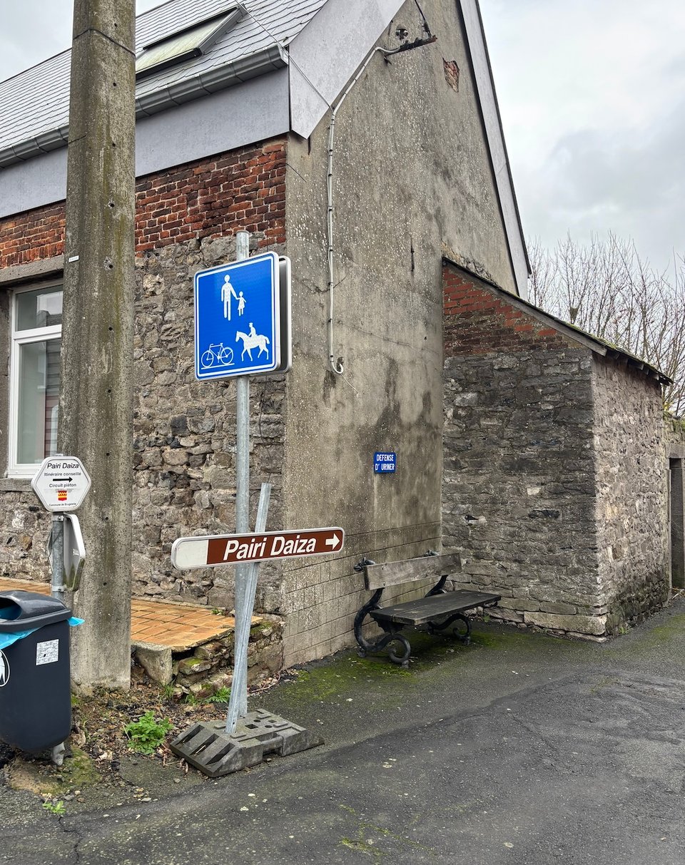 A picture of a sign reading PAIRI DAIZA pointing down an alleyway past a bench