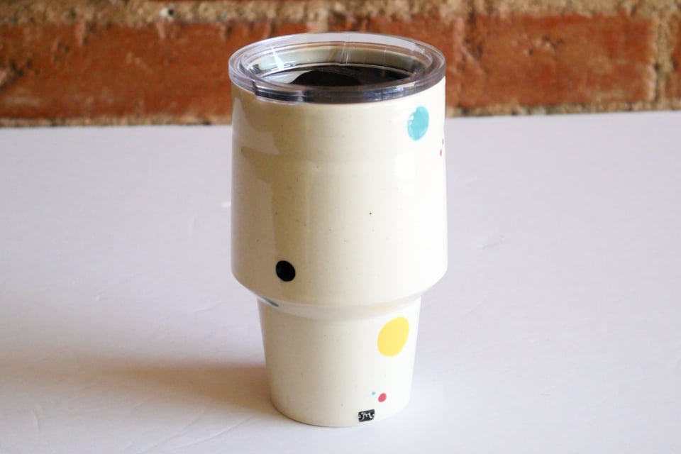 Angular White tumbler with a narrow cup-holder-friendly base that flares slightly in the first couple inches, and then angles out more dramatically, and slopes gently back in towards the vertical lip. A travel lid fits snug at the top.