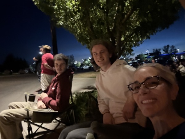 A dark and blurry image of three people sitting in camp chairs under a tree waiting for fireworks to start