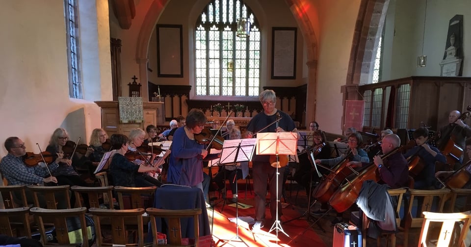 An orchestra rehearsing inside the church, two soloists (violin and viola) are in the centre