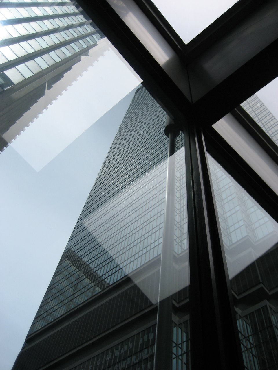 A building is reflected in or seen through glass supported by black beams.