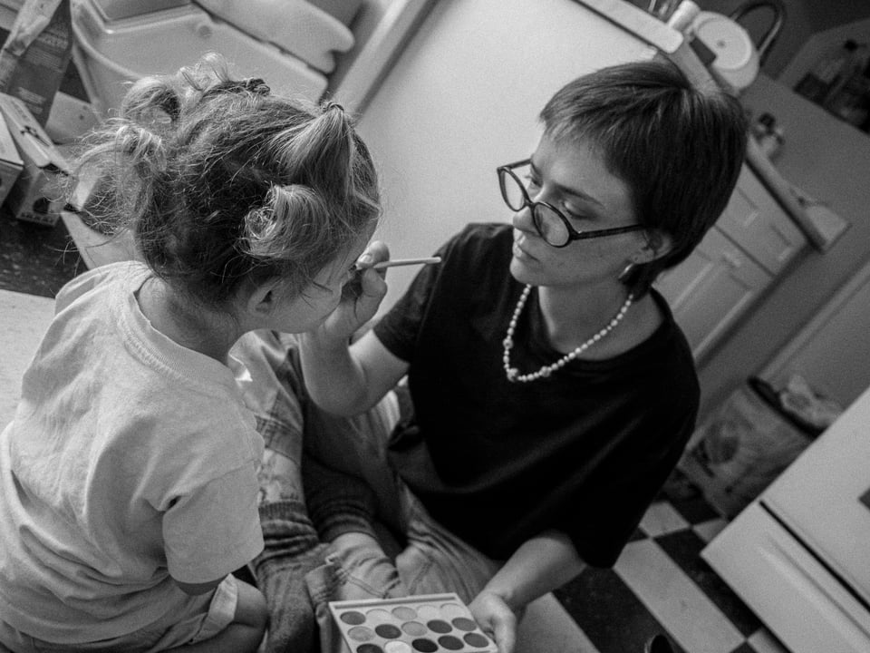 A white woman, Bonnie, painting a kitty face on my kiddo, Sona.
