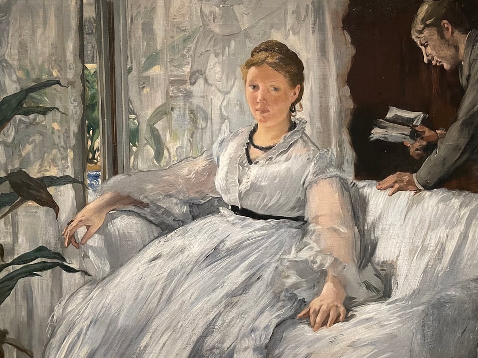 Manet's partner Suzanne in a flowing white dress seated on a couch, with her son Leon holding a book behind her.