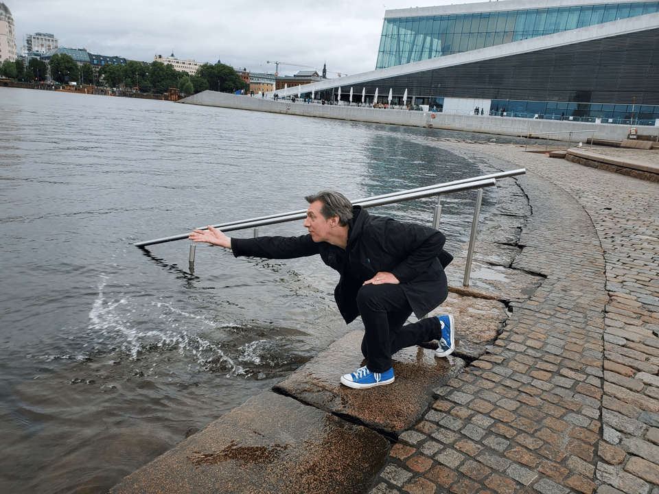 A crouched man splashes water with an opera house in the background