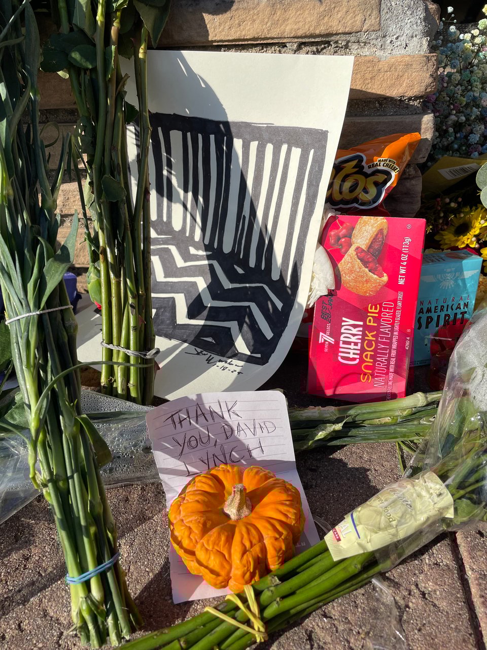 A small rotting pumpkin with a note that reads Thanks You, David Lynch next to flowers, artwork, and cherry pie
