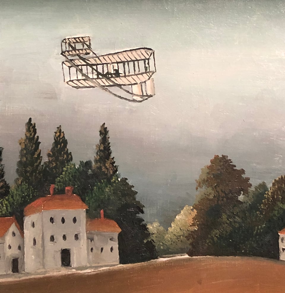 Detail of a very simple aircraft flying above buildings and trees.