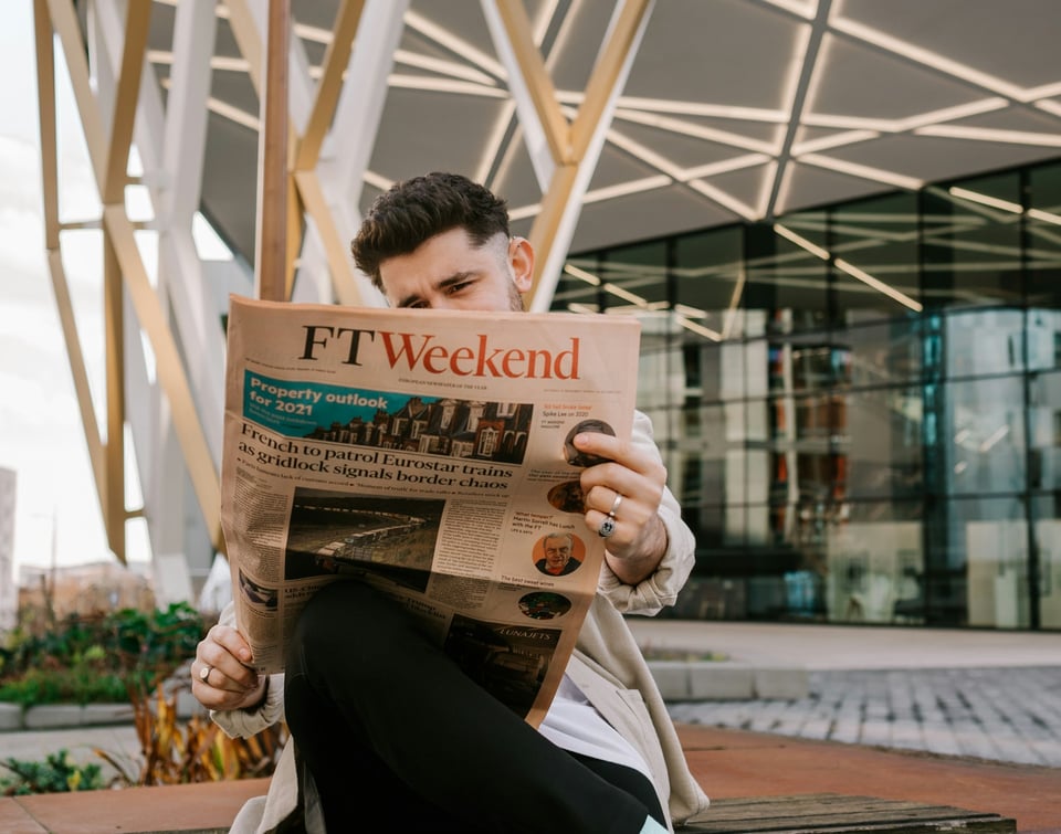 A man, seated, reading a copy of the Financial Times FT Weekend section. Photo by Toa Heftiba on Unsplash