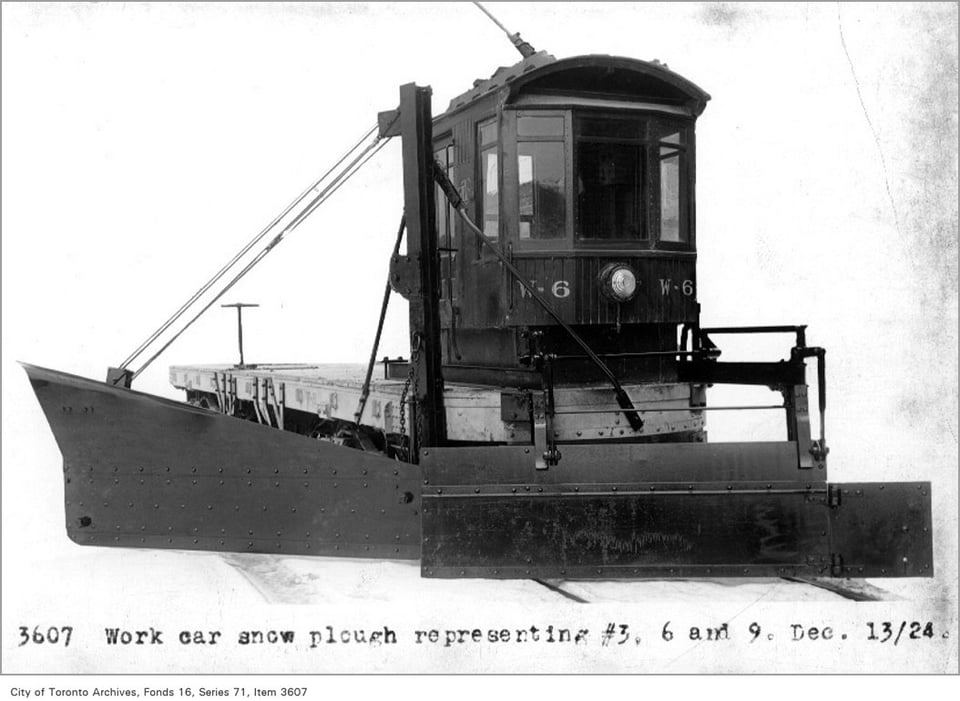 image of a very early-1900s vehicle (little train cabin, riveted metal) pushing a plow down some rails