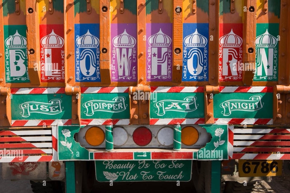Back of an Indian truck with three messages painted in miriad of colours, and decorated ornamentally. They read 'Blow horn', 'Use dipper at night', and 'Beauty is to see, not to touch'.