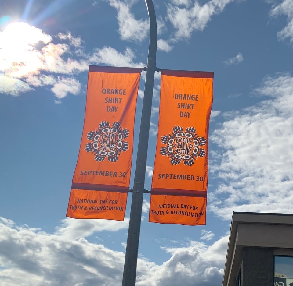Two orange banners on a lightpost against a mostly sunny day, showing Orange Shirt Day (Every Child Matters) and National Day for Truth & Reconciliation