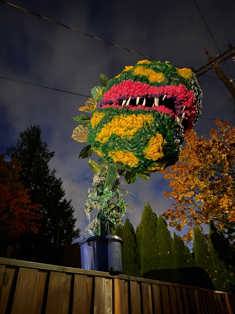 A tall DIY sculpture of Audrey 2 from Little Shop of Horrors, a giant singing plant with lipstick and sharp teeth. It's sitting on top of a fence
