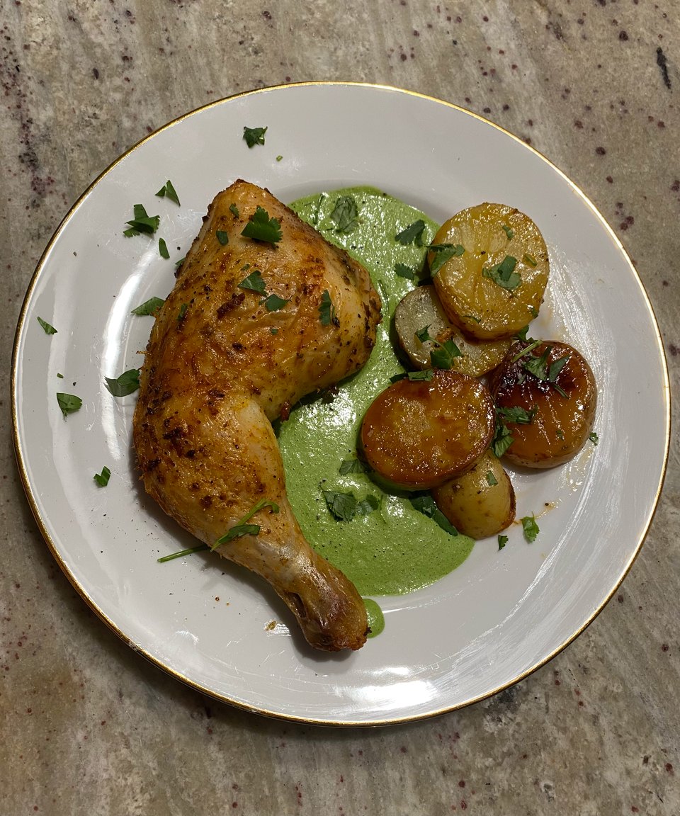 Chicken quarter with potatoes laid on top of a green sauce and sprinkled with cilantro.