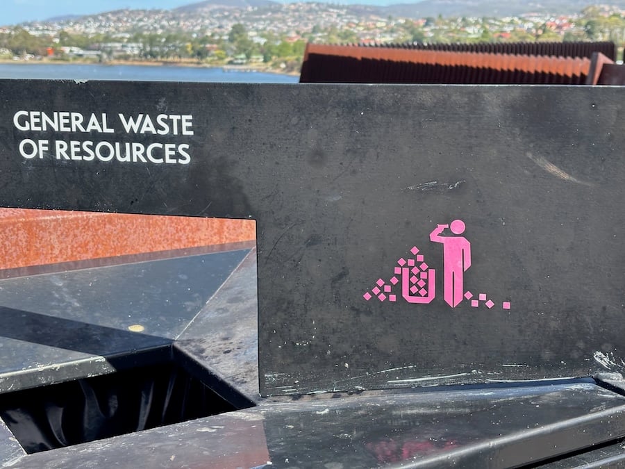 This is a photo of a rubbish bin, taken at MONA. Written over the bin is "GENERAL WASTE OF RESOURCES" and there's a picture of a little guy saluting or drinking while surrounded by a pile of rubbish.