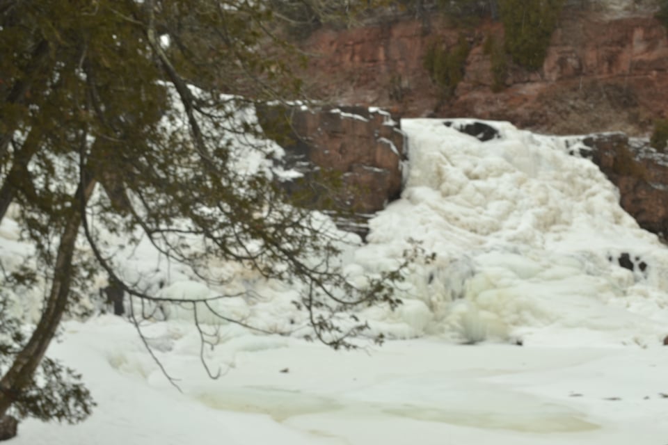 Ice tumbles over a cliff, with red rock behind it.