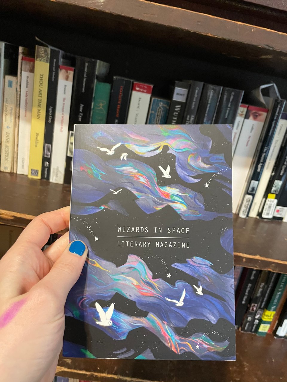 Wizards in Space issue nine cover, white owls flying through the aurora borealis, my hand is in shot and you can see my blue nail polish and the smudge of purple ink on my thumb from filling up a fountain pen