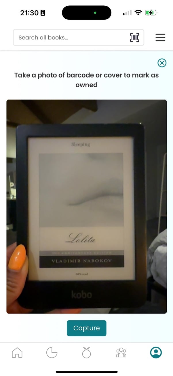 Screenshot from my phone of me holding up my Kobo to the new barcode scanner. The Kobo is "Sleeping" and a cover of Nabokov's "Lolita" is on display.
