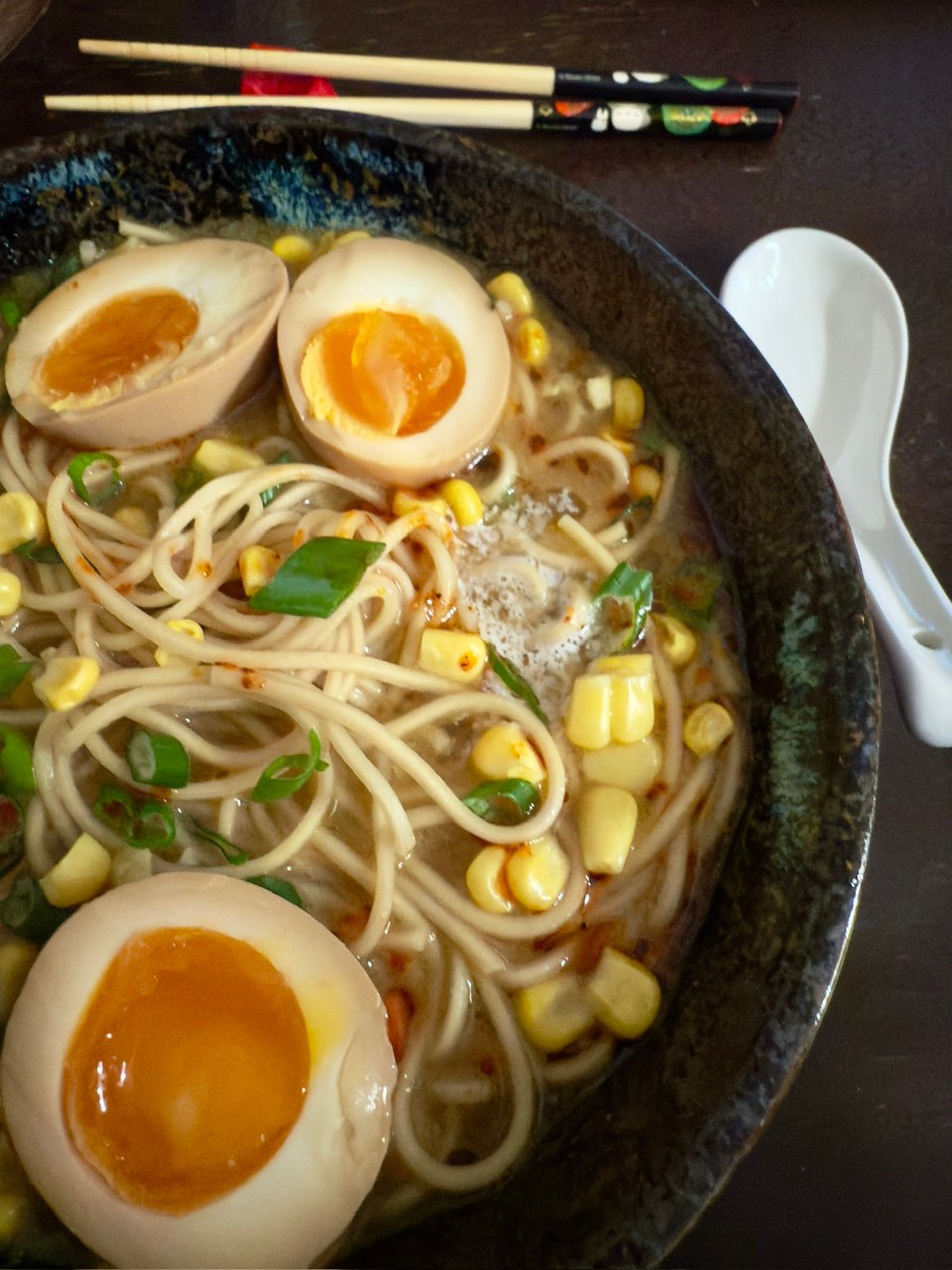 Soy sauce marinated jammy eggs on top of a bowl of ramen noodles with corn and scallions in a miso broth.