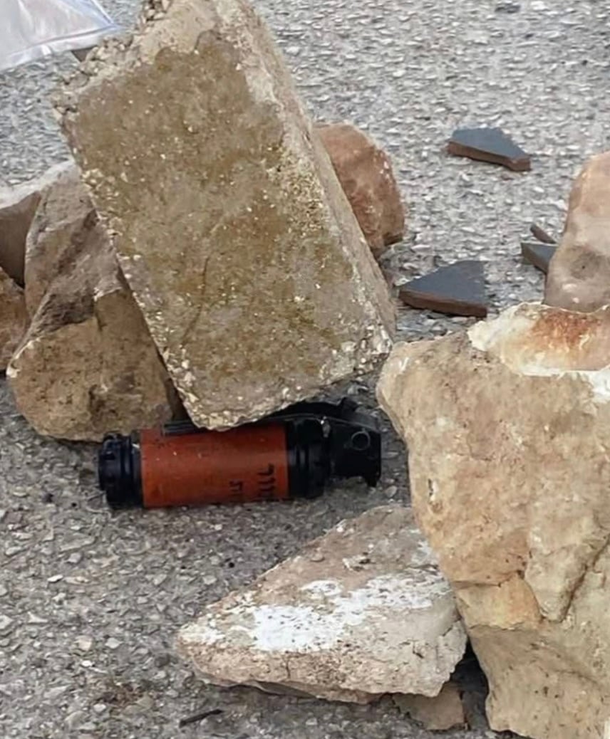 A pile of rocks on the street, with a brown and black cannister with Hebrew writing