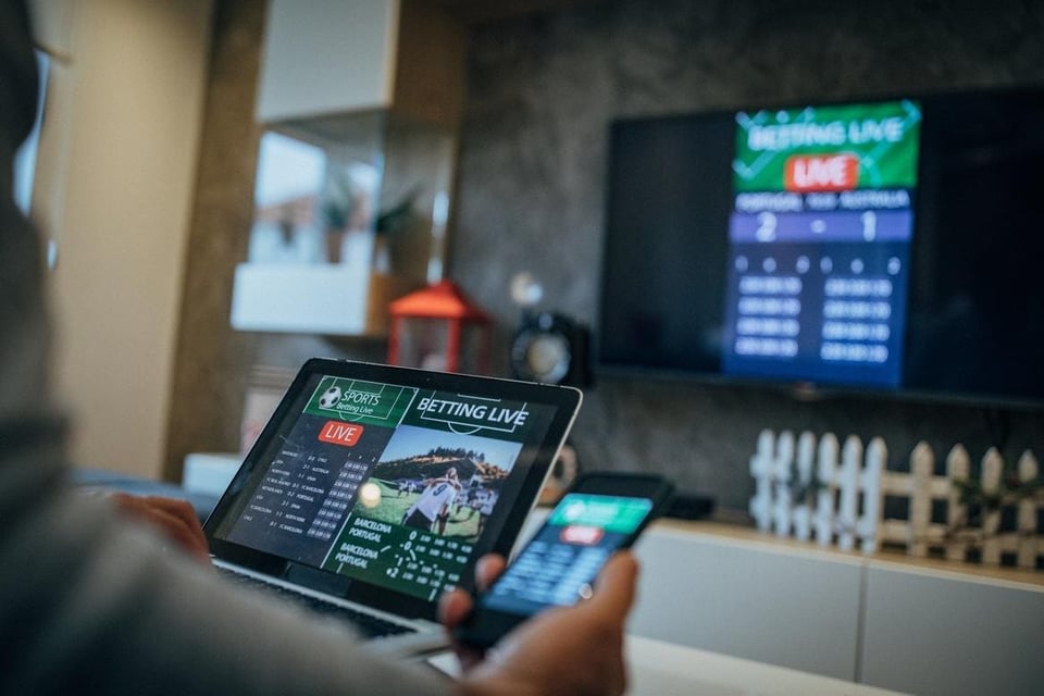 Image of a dude, always a dude, with three devices showing them sportsbetting options