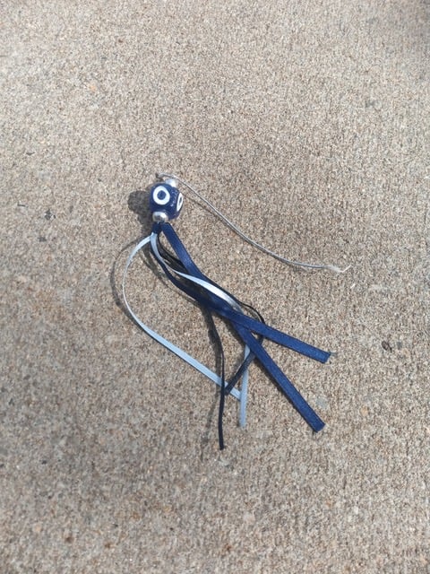 A glass bead decorated with a blue circle in a white circle (aka, the evil eye), with blue and white ribbons adorning it