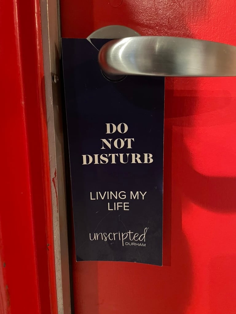 A sign hangs from the handle of a bright red door at a hotel. The sign reads DO NOT DISTURB. LIVING MY LIFE.