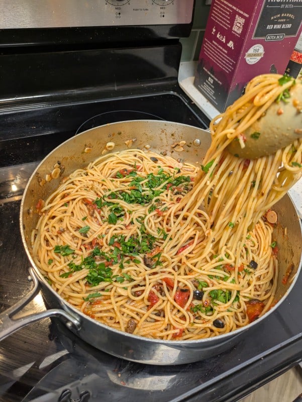 a pair of tongs pulls spaghetti out of a high-walled pan