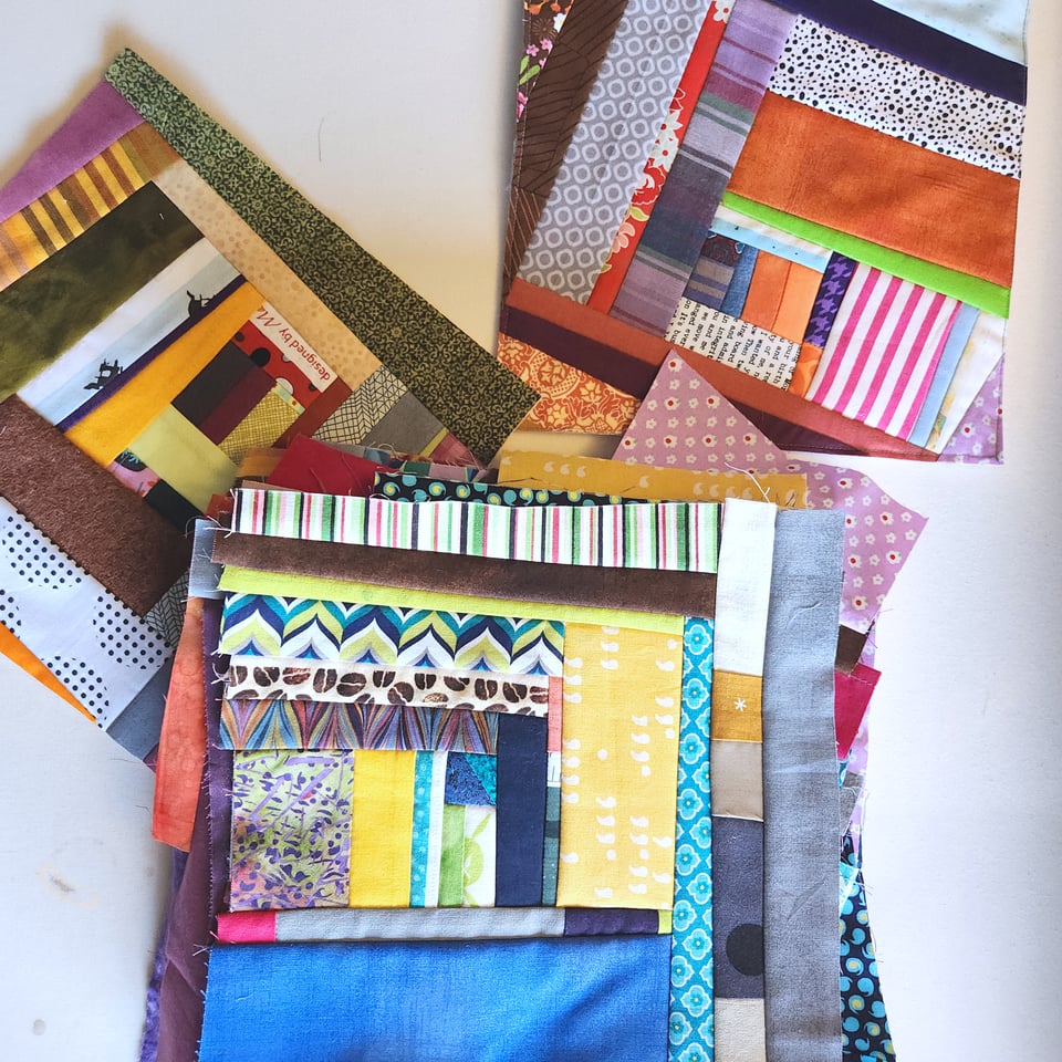 Photo of Sarah's quilted potholders in progress. There are 3 overlapping stacks of squares composed of fabric scraps in every color.