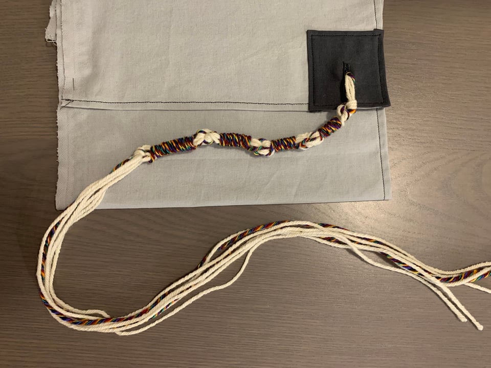 a large rainbow and white sample tzitzit tied onto a corner.