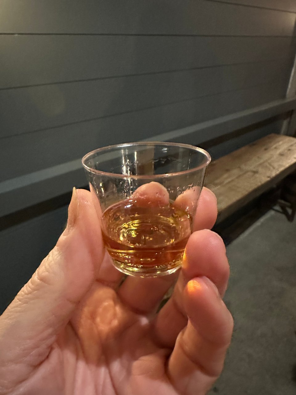 photo of a hand holding a clear plastic tasting-cup of bourbon
