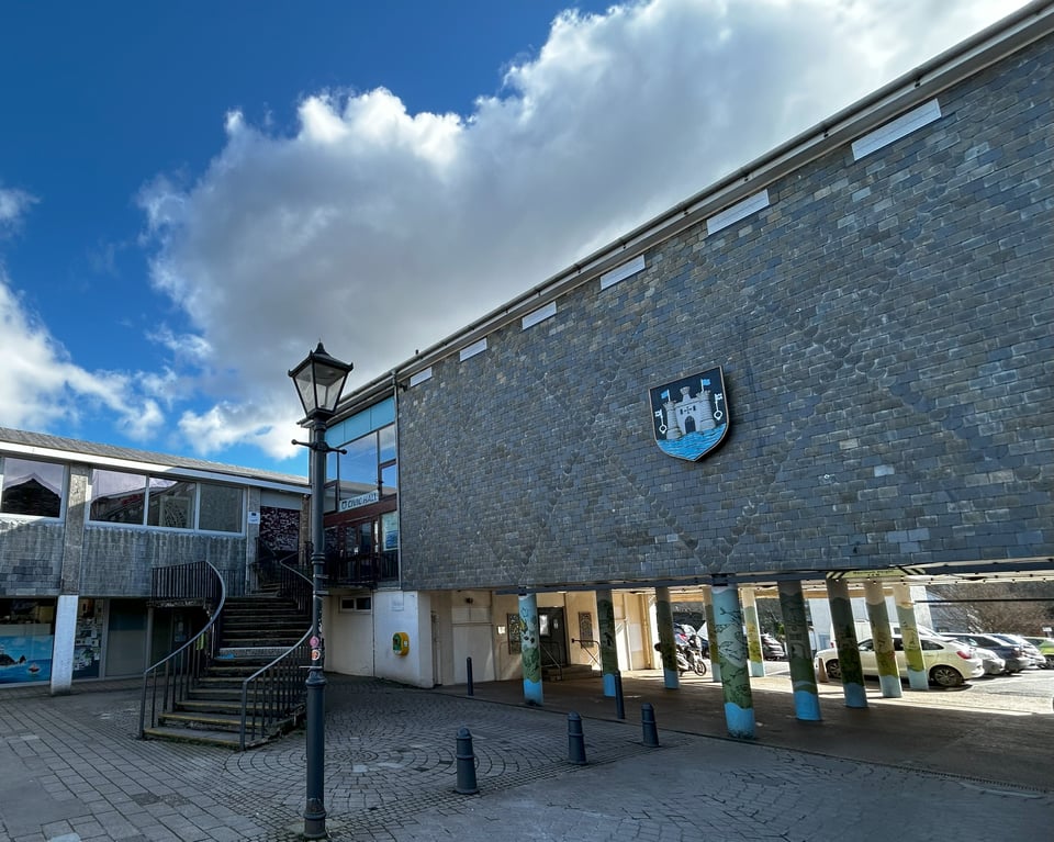 The bulk of the Civic Hall with the curved staircase. It's a large mass, with glass fronting the foyer but an otherwise blank wall of slates in which faint traces of the large X patterns are just visible. Someone has stuck a large town crest on it.To the left is the later annex.